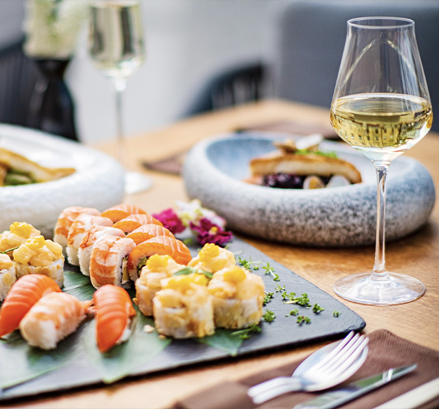 Tabla de sushi variado con nigiris y rolls maridado con una copa de vino blanco fresco en un restaurante.