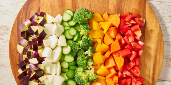 Tabla de cortar de madera con verduras variadas cortadas de forma uniforme en cubos y láminas con mandolina de cocina